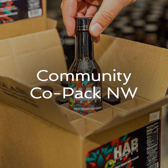 A photo showing a bottle being pulled out of a cardboard box. Overlaying text reads "Community Co-Pack NW"